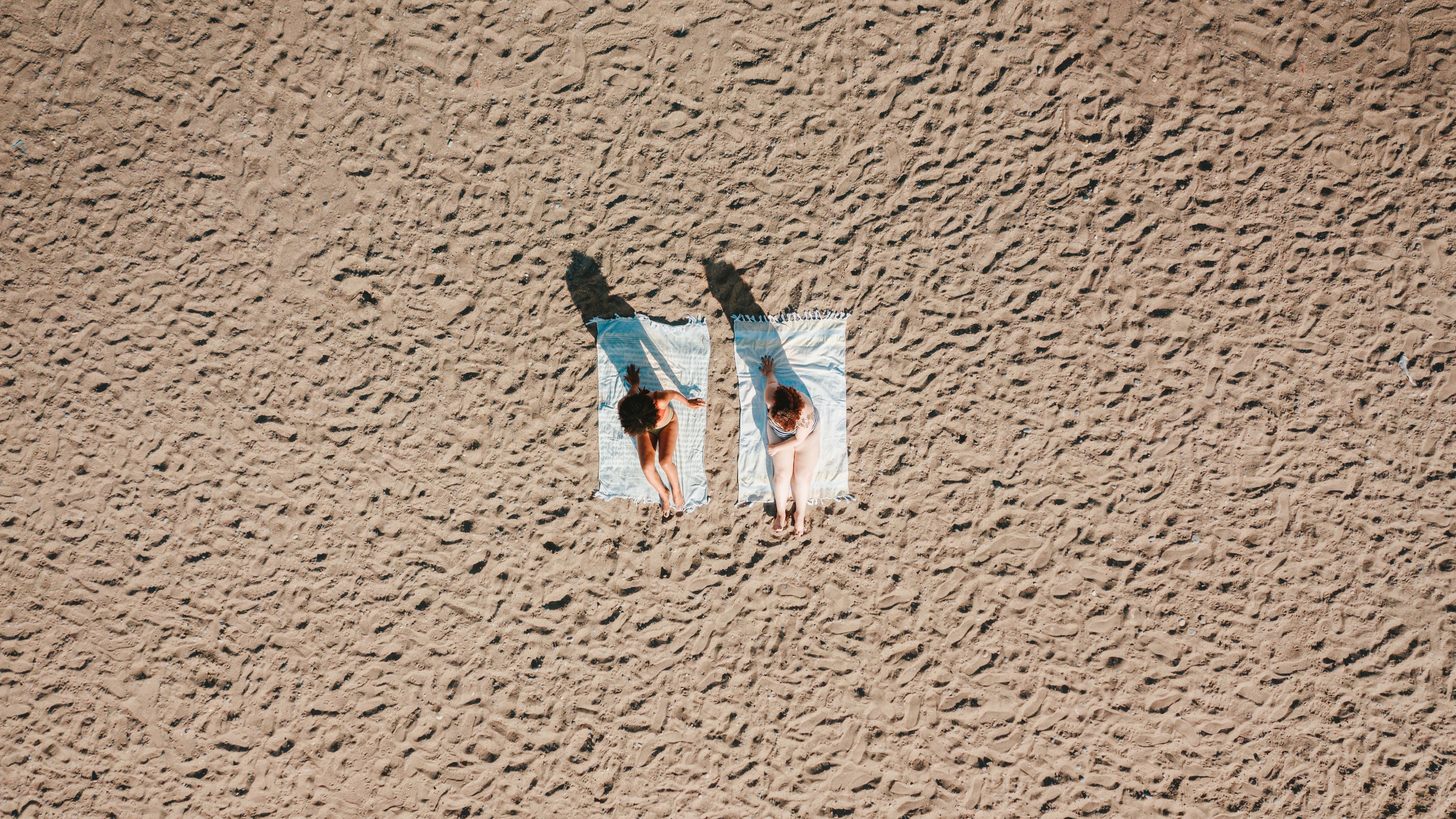 Two women lying on the beach with Cove & Curve swimwear branding — sculpting swimwear designed for DD+ cup sizes, curves, and confidence.